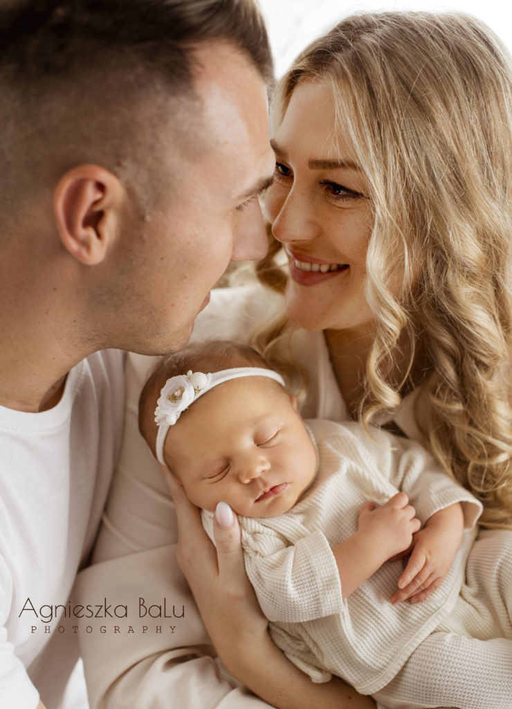 Die glückliche Ehe. Die Mama guckt tief in Papasaugen. Die Eltern halten das Baby auf der Arm. Die Mama lächelt.