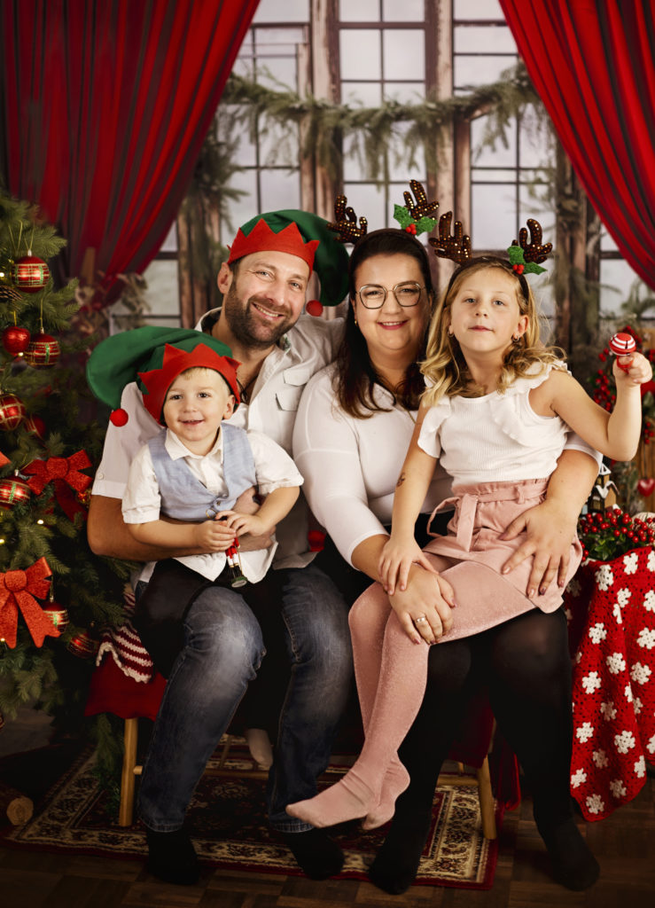 Ein Familie sitzt auf die Bank und trägt die Weihnachtsmützen. Daneben ist ein Tannenbaum zu sehen.