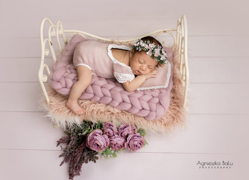 Das Pastelbild von dem Neugeborenen, die auf einem rosa Bett schläft und ein passendes Outfit trägt.