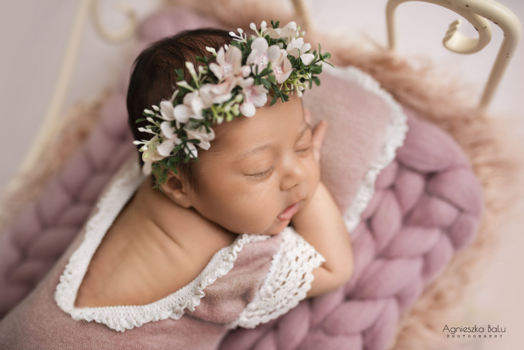 Das Baby mit dem Blumenstirnband liegt auf die rosa Decke und dem rosa Kissen. Im Focus sind die Babiesaugen.