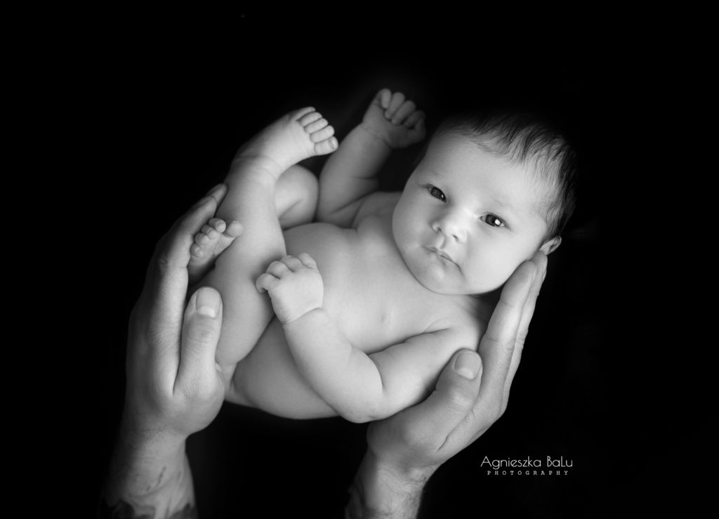Das Schwarz-Weiß Bilder von dem Neugeborenen. Das Baby ist durch die Papashänden unterstützt.
