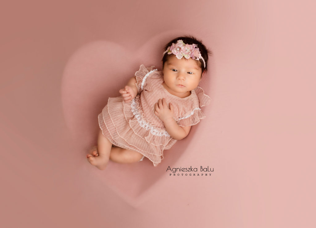 Natürliches Bild von dem Baby, das auf die rosa Decke liegt. Dahinter befindet sich das Herz. Das Baby hat die Augen auf.