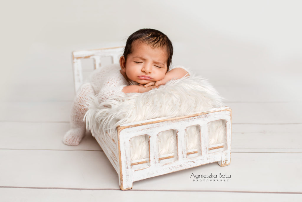 Die Fotografie von dem schlafenden Baby. Der Boden, die Decken als auch die Babieskleidung sind weiß. Natürliche Fotografie.