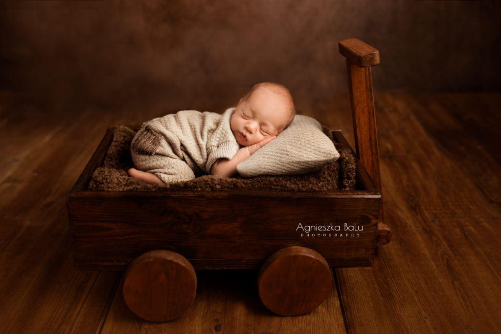 Das Vintagebild von dem Baby, die beige Kleidung trägt und in den Holzwagen schläft.
