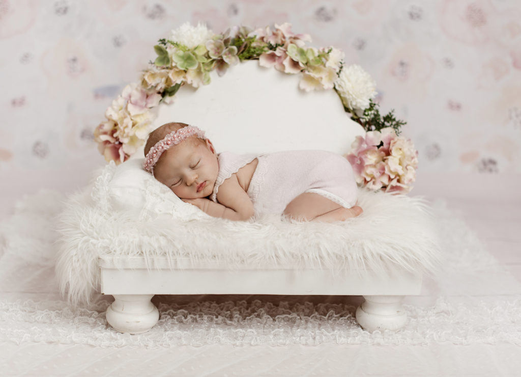 Das Baby liegt auf dem Mädchenbett und ist während Babyshooting in Berlin fotografiert. Die Pastefarben von dem Hintergrund und die Decke passen zum Rosaoutfit des Babies.
