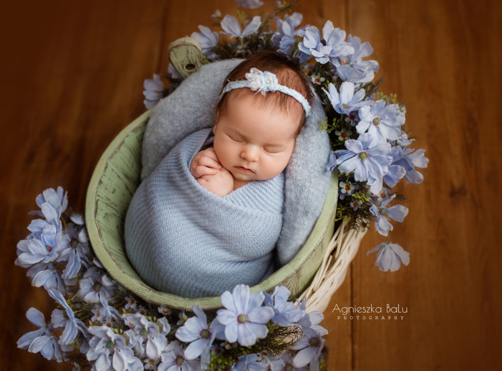 Das Babymädchen ist von blauen Tuch gepuckt und liegt zwischen den Blumen.
