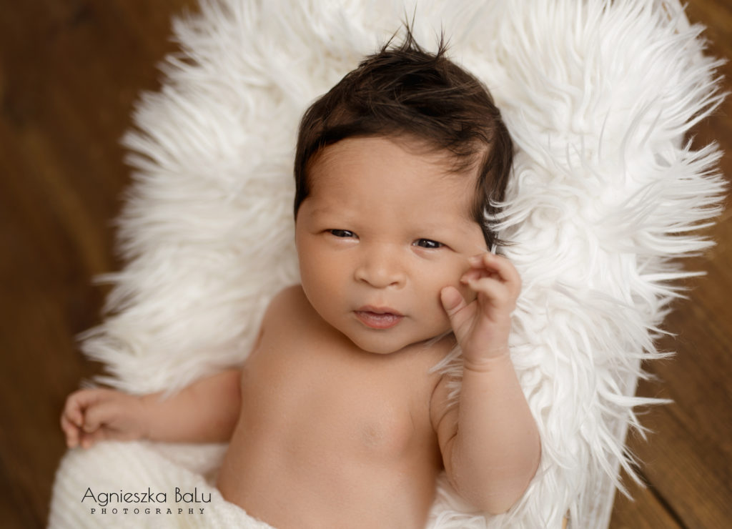 Eine natürliche Fotografie von dem Baby auf die weiße Decke. Das Baby guckt schön in die Kamera und hält die Auge breit offen.