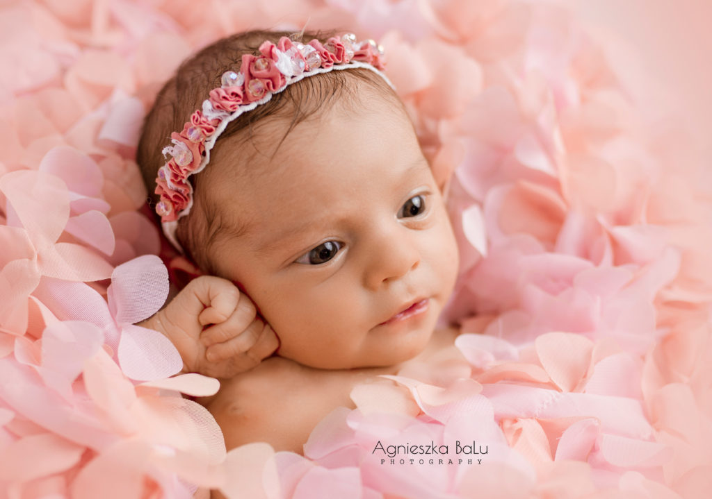 Das kleine Babymädchen unterstützt ihre Kopt mit der kleinen Fautschen. Ihre Augen sind groß. Sie liegt in den rosa Blumen.