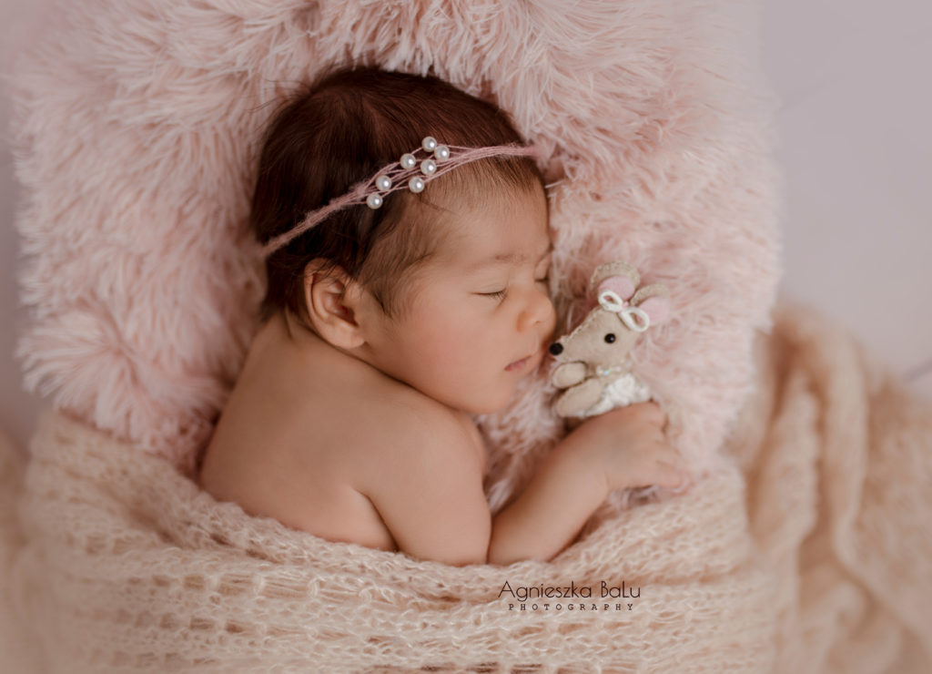 Das Neugeborenene mit dem Kuscheltier schläft auf die rosa Decke während des Fotoshooting in Berlin.
